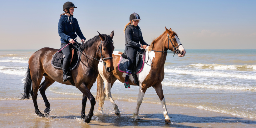 Reitschüler beim Reiten am Strand mit ihren Pferden