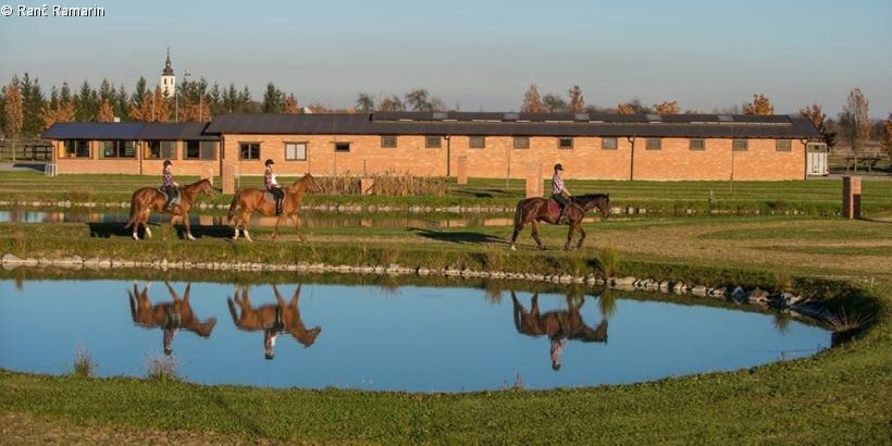 Reiter spiegeln sich im Teich vor dem Pferdehof Ranč Ramarin in Slawonien