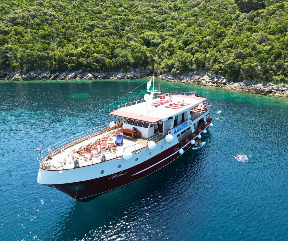 Motoryacht MY Vilma vor Anker in einer türkisblauen Bucht – Gäste entspannen an Deck oder genießen das Bad im klaren Meer.