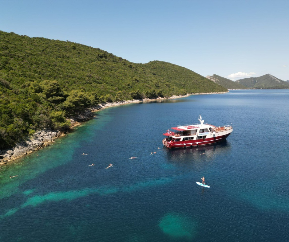 Die MY Vilma ankert in einer türkisblauen Bucht – Gäste schwimmen und paddeln rund um das Schiff.