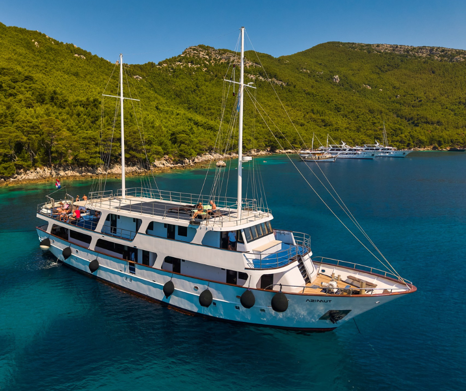 MS Azimut liegt vor Anker in einer türkisblauen Bucht, umgeben von grüner Küste Dalmatiens. 