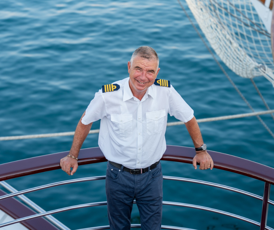 Kapitän Silvio Vuković steht lächelnd an der Reling des Schiffes MY Vita, umkreist vom tiefblauen Meer.
