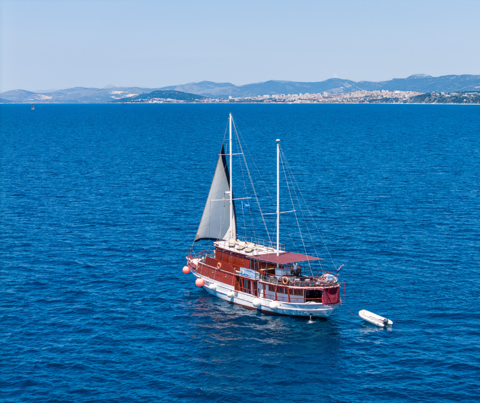 Das Schiff MS Mirabela unter Segeln auf offenem Meer, im Hintergrund die Küste Dalmatiens.