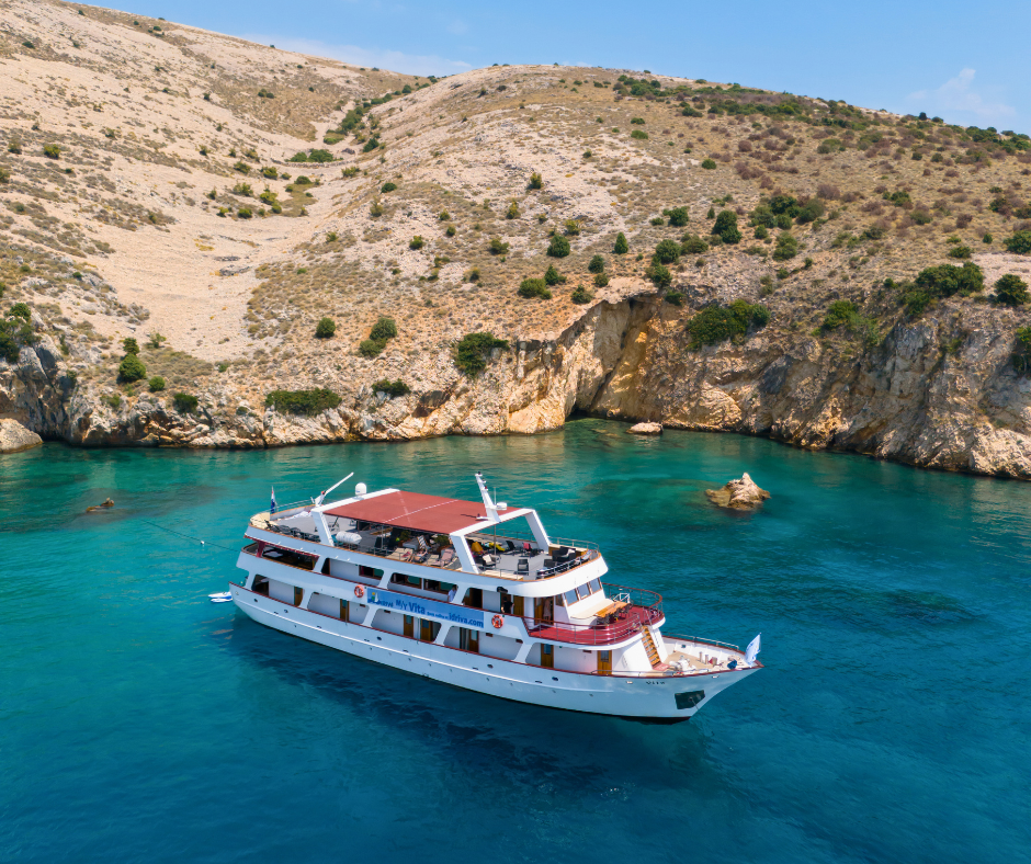 Die Motoryacht Vita liegt in einer ruhigen Bucht mit türkisblauem Wasser, vor felsiger Küstenlandschaft.